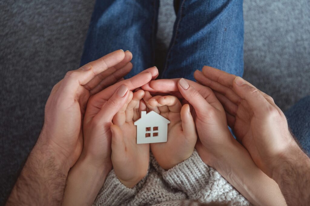 A family's hands holding a house model in the concept of relocating.